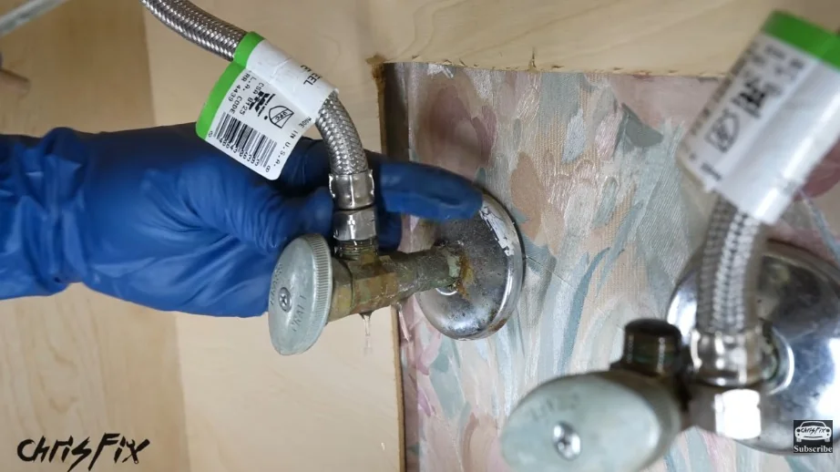 Gloved hand checking a shutoff valve and supply lines